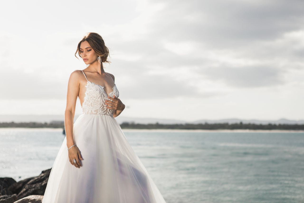 services-04 A beautiful bride in a stylish wedding dress posing by the ocean under soft daylight.
